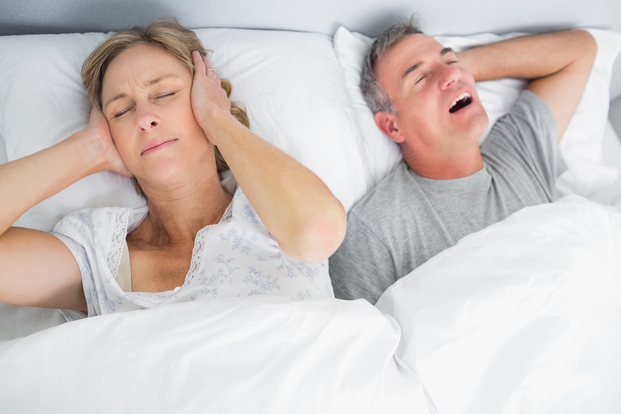 Wife blocking her ears from noise of husband snoring in bedroom